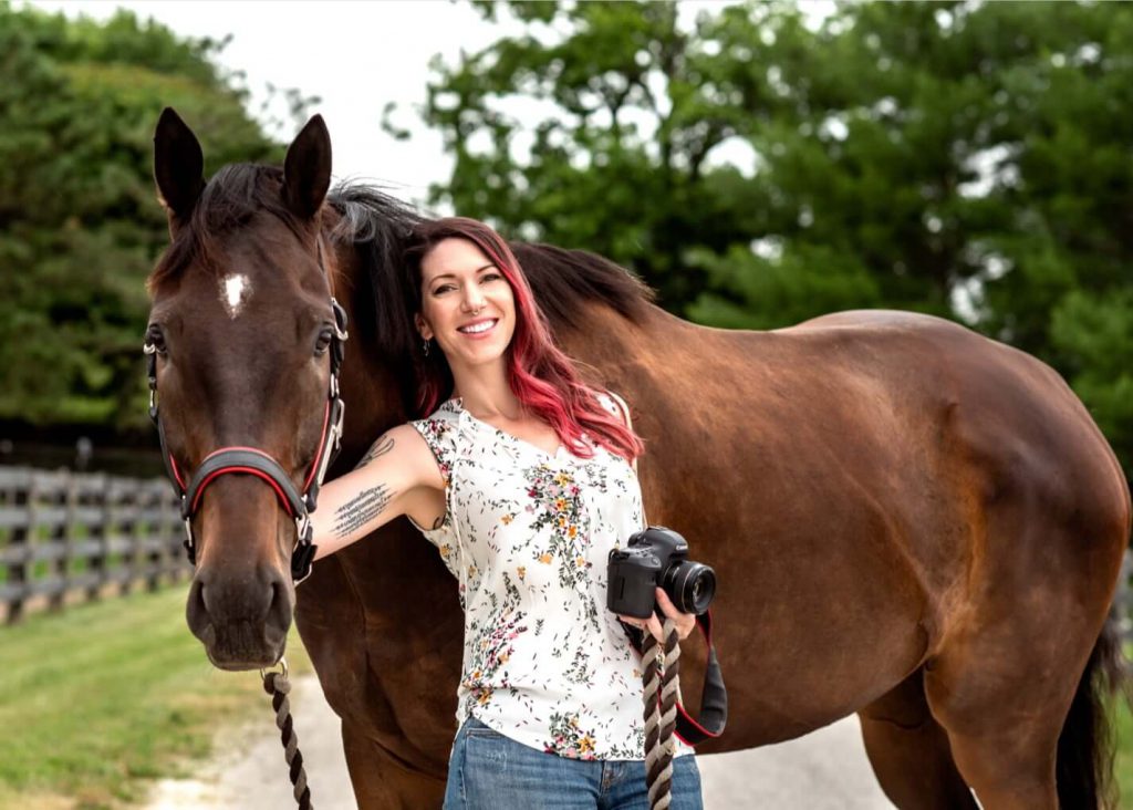 Woman with holding camera standing next to horse